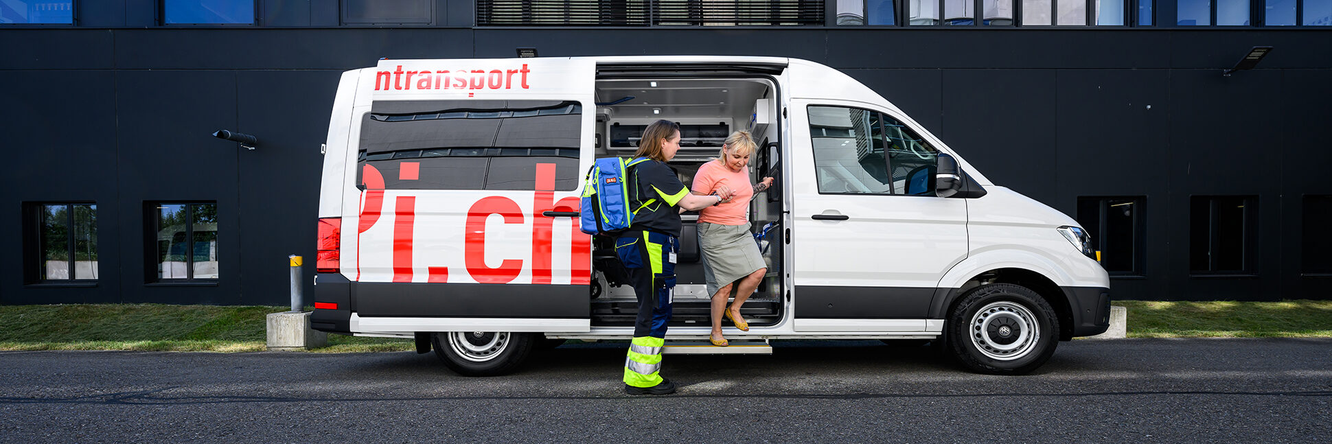 A staff member accompanying a seated patient to the transport vehicle